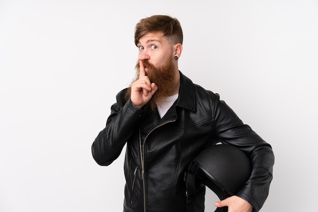 Hombre pelirrojo con barba larga sosteniendo un casco de motocicleta sobre pared blanca aislada haciendo gesto de silencio