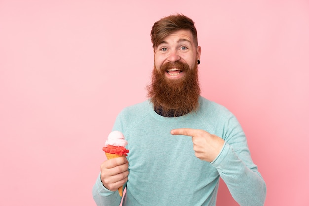Hombre pelirrojo con barba larga sosteniendo un helado de cucurucho sobre rosa aislado con expresión facial sorpresa