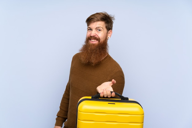 Hombre pelirrojo con barba larga sosteniendo una maleta con expresión triste