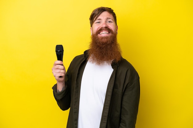 Hombre pelirrojo con barba recogiendo un micrófono aislado de fondo amarillo sonriendo mucho