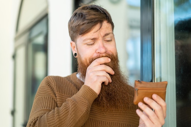 Hombre pelirrojo con barba sosteniendo una billetera y mirándola