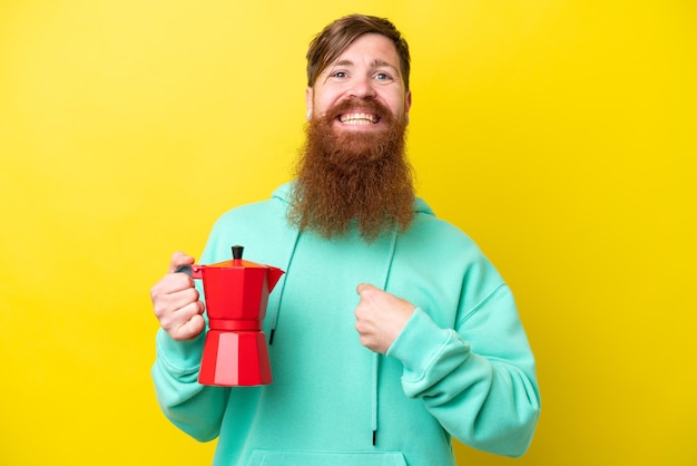 Hombre pelirrojo con barba sosteniendo una cafetera aislada de fondo amarillo con expresión facial sorpresa