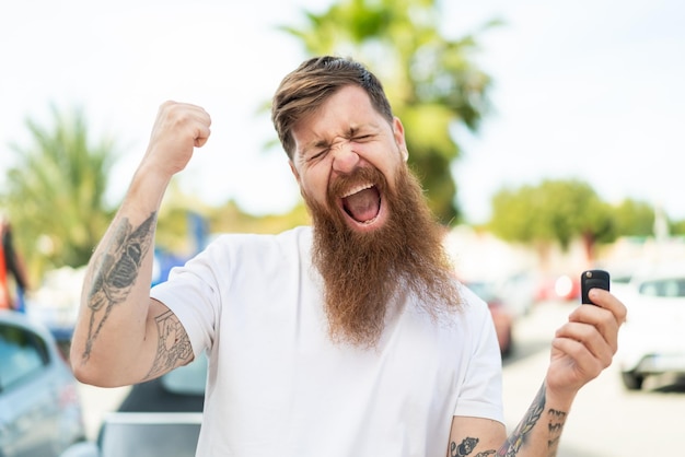 Hombre pelirrojo con barba sosteniendo las llaves del auto y celebrando una victoria