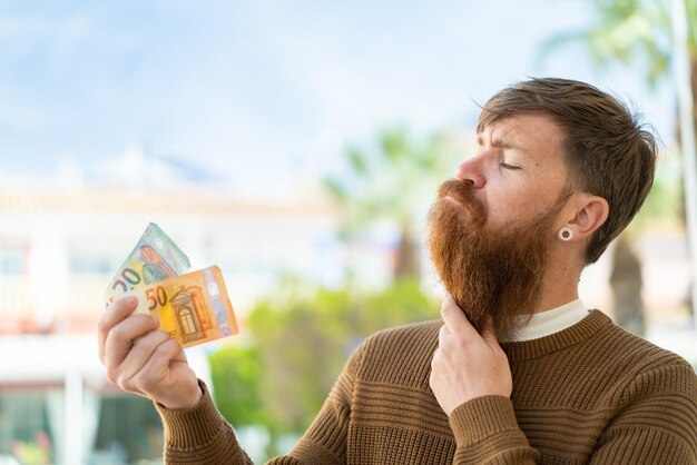 Hombre pelirrojo con barba tomando mucho dinero al aire libre