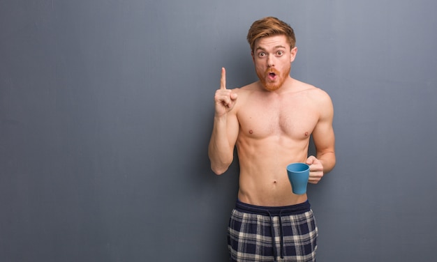 Hombre pelirrojo sin camisa joven que tiene una gran idea, concepto de creatividad. Él está sosteniendo una taza de café.