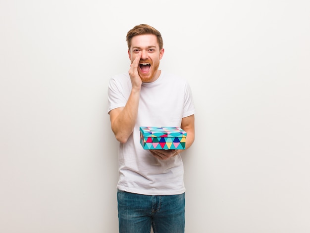 Hombre pelirrojo joven gritando algo feliz al frente. Sosteniendo una caja de regalo.