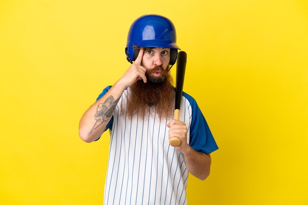 Hombre pelirrojo jugador de béisbol con casco y bate aislado sobre fondo amarillo pensando en una idea