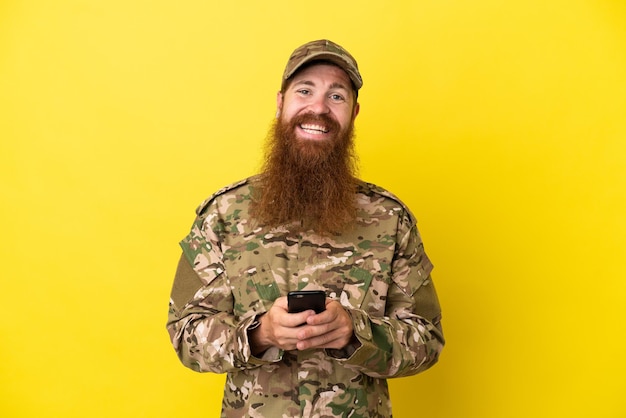 Hombre pelirrojo militar más aislado sobre fondo amarillo enviando un mensaje con el móvil