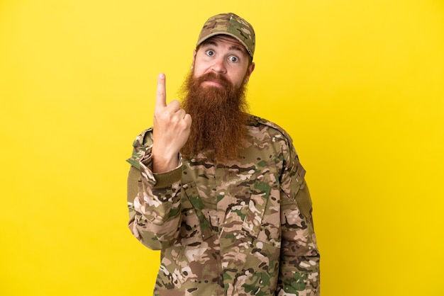 Hombre pelirrojo militar sobre aislado sobre fondo amarillo apuntando con el dedo índice una gran idea