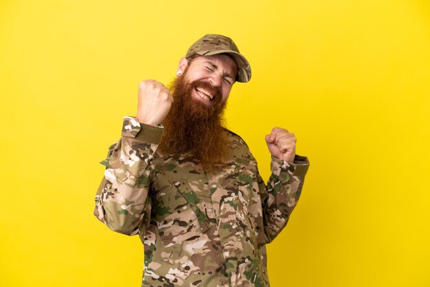Foto hombre pelirrojo militar sobre aislado sobre fondo amarillo celebrando una victoria