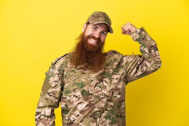 Foto hombre pelirrojo militar sobre aislado sobre fondo amarillo haciendo gesto fuerte