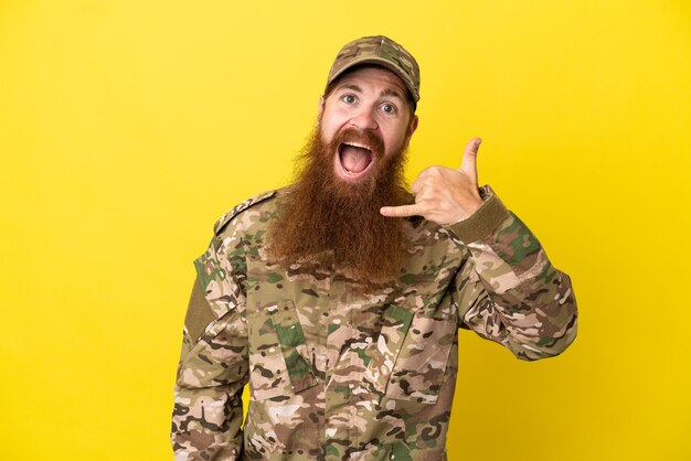 Hombre pelirrojo militar sobre aislado sobre fondo amarillo haciendo gesto de teléfono. Llámame señal