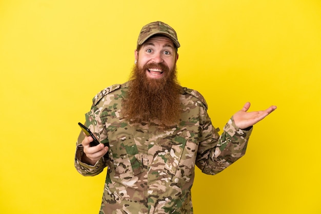 Hombre pelirrojo militar sobre aislado sobre fondo amarillo manteniendo una conversación con el teléfono móvil con alguien