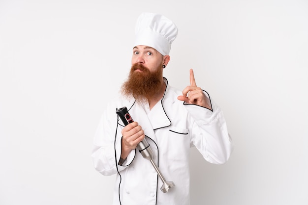 Hombre pelirrojo que usa la batidora de mano sobre una pared blanca aislada que señala con el dedo índice una gran idea