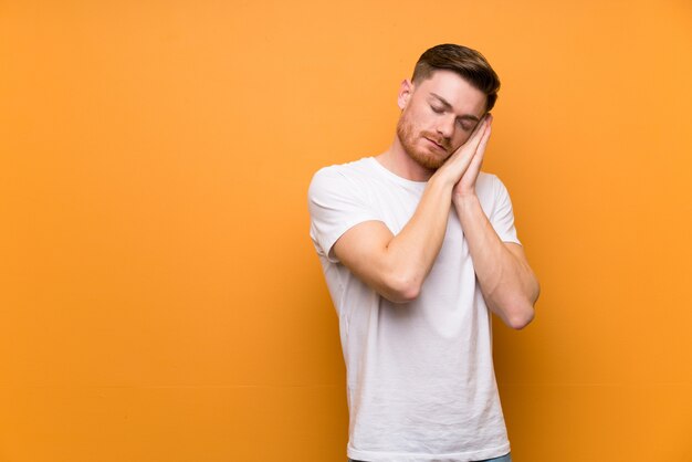 Hombre pelirrojo sobre pared marrón haciendo gesto de sueño en expresión adorable