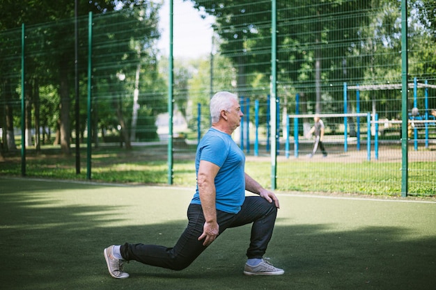 hombre de pelo gris de 50 años haciendo un calentamiento en una cancha deportiva en el parque