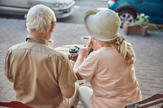 Hombre de pelo gris y una dama en un sombrero para el sol sentados en un café