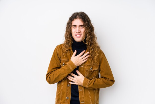 Hombre de pelo largo posando aislado se ríe alegremente y se divierte manteniendo las manos sobre el estómago.