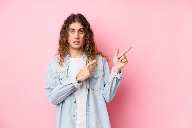 Hombre de pelo largo posando aislado sorprendido apuntando con los dedos índices a un espacio de copia.