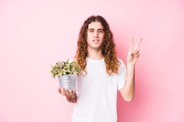 Hombre de pelo largo sosteniendo una planta que muestra el número dos con los dedos