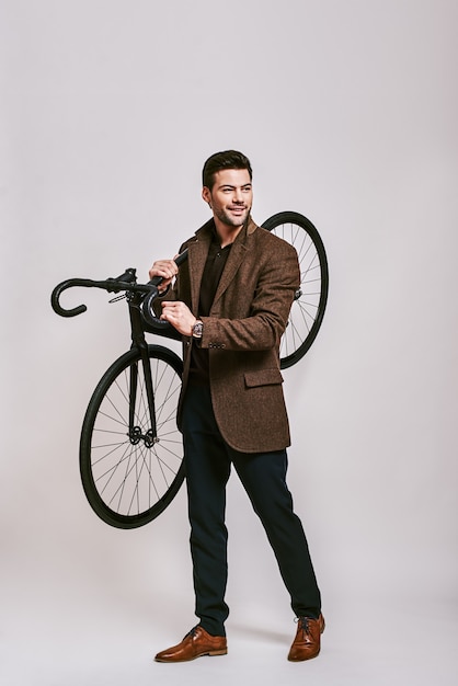 Hombre de pelo oscuro con estilo ecológico que sostiene la bicicleta en sus manos sonriendo y mirando