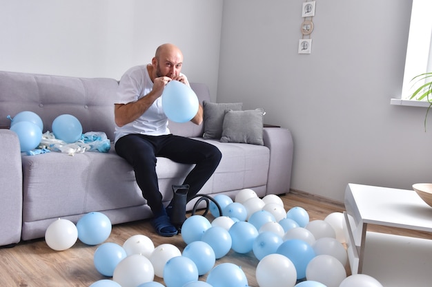 Hombre sin pelo que sopla globos azules y blancos