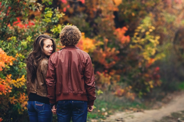 El hombre de pelo rizado le dio la espalda y la chica se asoma por detrás de su hombro. pareja amorosa en hermosos árboles coloridos del otoño.