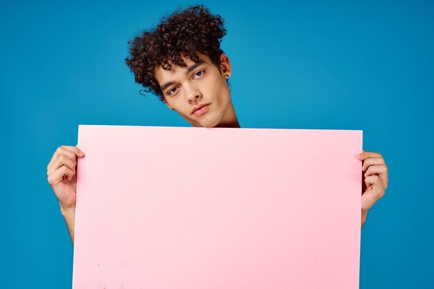 Hombre con pelo rizado sosteniendo cartel rosa banner fondo azul