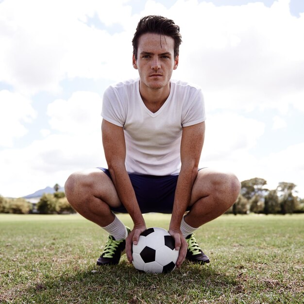 Hombre pelota de fútbol y retrato en el suelo para el deporte con orgullo confianza y listo para el desafío en el campo persona atleta y jugador de fútbol en el césped para el ejercicio entrenamiento y entrenamiento para el juego