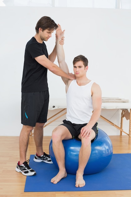 Hombre en la pelota de yoga trabajando con un fisioterapeuta