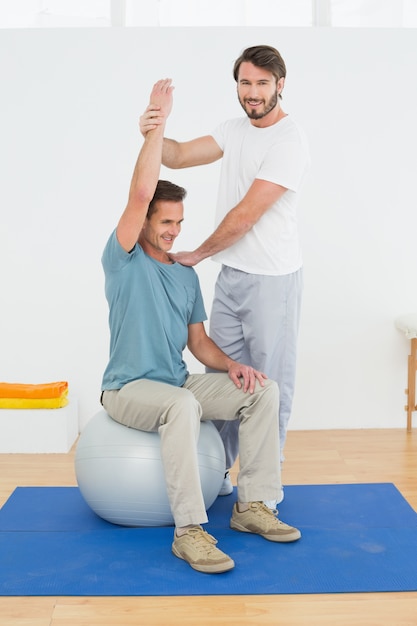 Hombre en la pelota de yoga trabajando con un fisioterapeuta