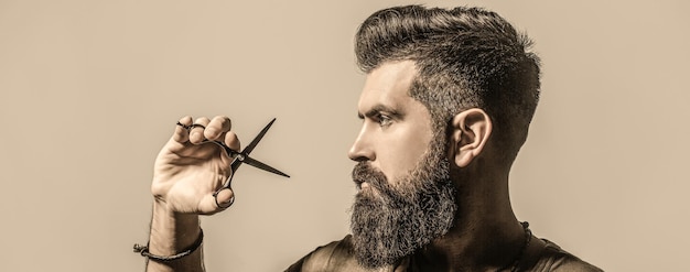 Hombre en peluquería, corte de pelo, afeitado. Hombre barbudo aislado sobre fondo gris. Mans corte de pelo en peluquería. Tijeras de peluquero, peluquería. Tijeras de peluquero. Barbería vintage, afeitado.