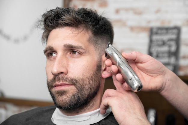 Hombre peluquero cortando el cabello de un cliente masculino con cortapelos en la peluquería Proceso de peinado Fotografía de alta calidad