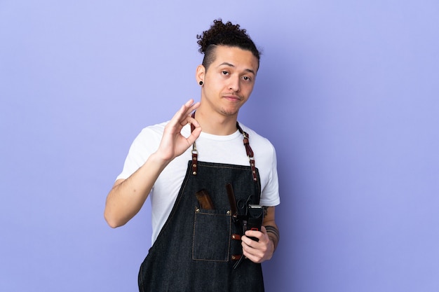 Foto hombre de peluquero en un delantal sobre púrpura aislado mostrando un signo de ok con los dedos