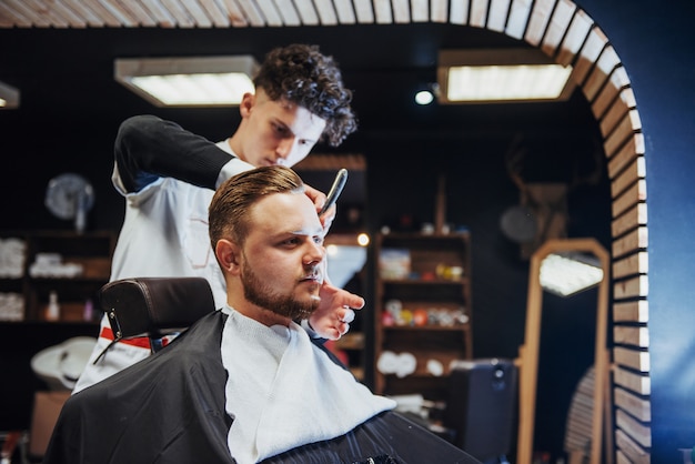 Hombre peluquero haciendo corte de pelo barba hombres adultos en la peluquería de hombres