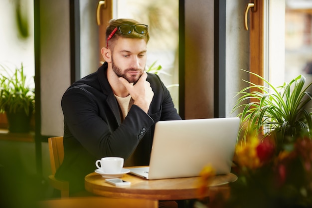 Hombre pensativo en la computadora portátil en el café