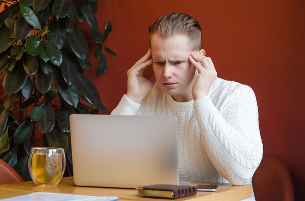 Hombre pensativo, estresado, molesto, mira fijamente a la computadora portátil, tenencias en la cabeza. trabajo remoto. teletrabajo noticias impactantes. quédate en casa. emociones humanas. crisis económica