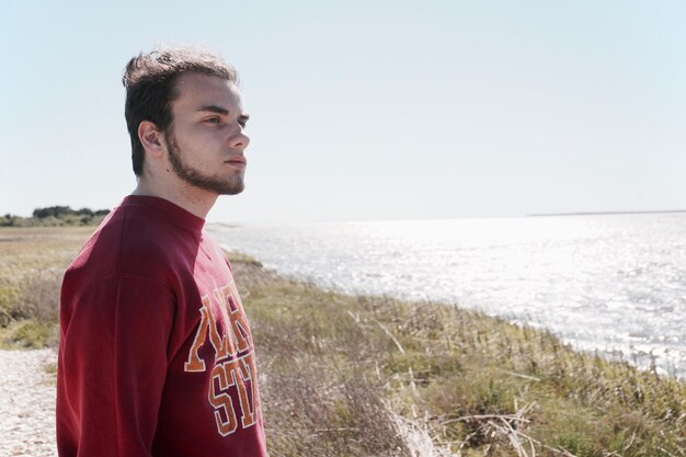 Hombre pensativo mirando hacia el mar contra el cielo despejado