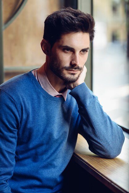 Foto hombre pensativo con suéter azul con mirada perdida cerca de una ventana