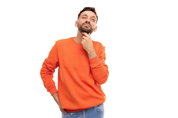 Un hombre pensativo con un suéter naranja se lleva la mano a la barbilla mirando cuidadosamente hacia arriba y hacia adelante.