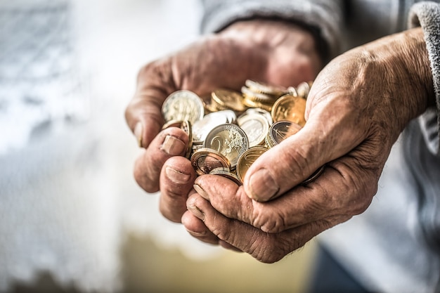 Hombre pensionista sosteniendo en las manos monedas de euro. Tema de pensiones bajas.