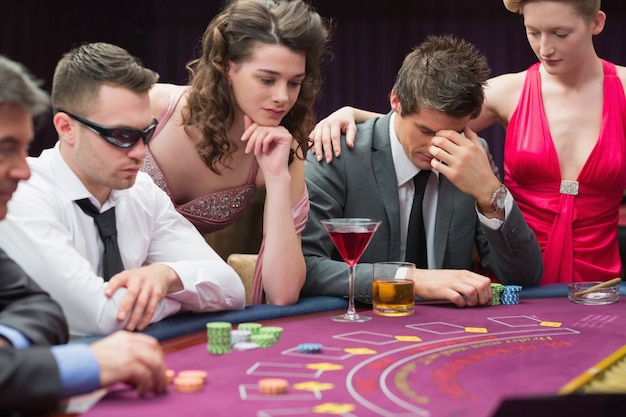 Hombre perdiendo en la mesa de póquer con la mujer consolándolo