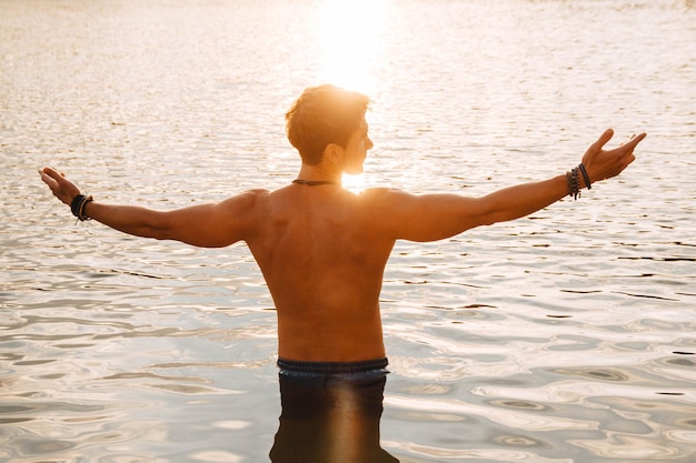 Hombre con perfectos soportes musculosos en el agua al atardecer arrojando sus manos a los lados