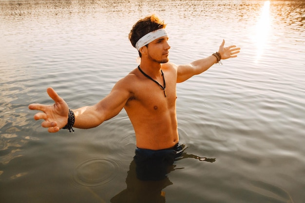 Hombre con perfectos soportes musculosos en el agua al atardecer arrojando sus manos a los lados