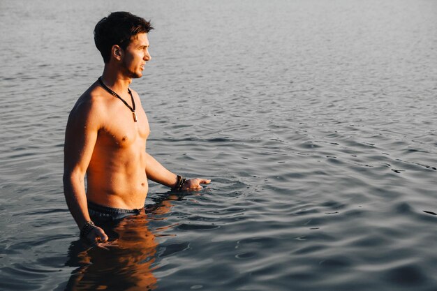 Hombre con perfectos soportes musculosos en el agua al atardecer. Lugar para texto o publicidad.