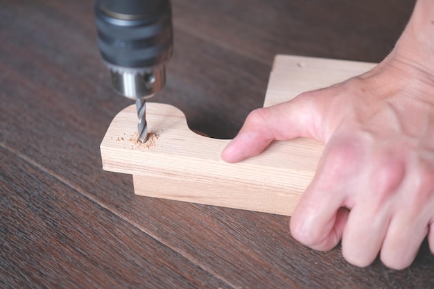 El hombre perfora un agujero en un detalle de madera con un taladro de cerca contra una superficie de madera