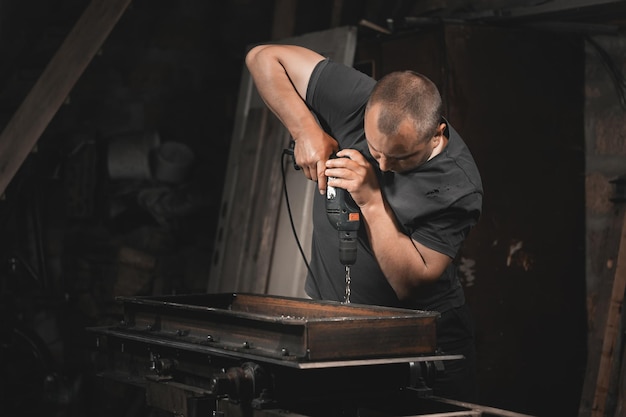 Foto un hombre perfora metal con un taladro manual en el taller de su casa fabricación de un producto de metal con sus propias manos