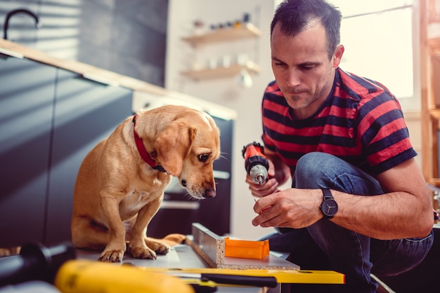 Hombre con perro construyendo armarios de cocina y utilizando un taladro inalámbrico