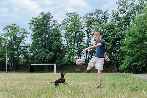 El hombre con un perro está jugando con una pelota de fútbol.