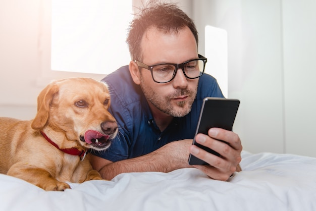 Hombre con el perro usando un teléfono inteligente en la cama